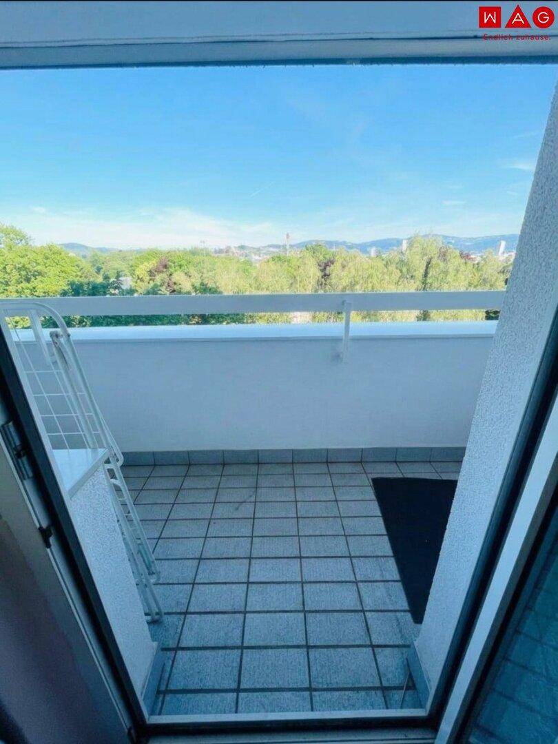 Weitläufiger Blick vom Balkon über grüne Baumwipfel und die umliegende Landschaft.