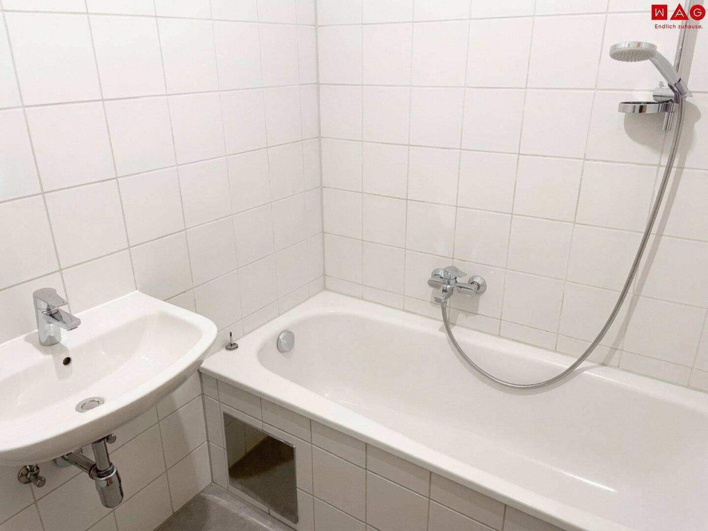 Funktionales Badezimmer mit Badewanne, Waschbecken und weißen Wandfliesen.