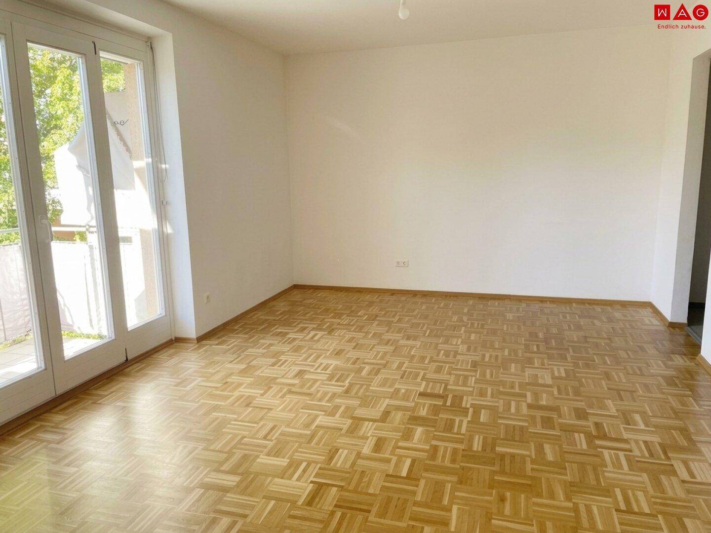Geräumiges Wohnzimmer mit Parkettboden und direktem Zugang zum Balkon.