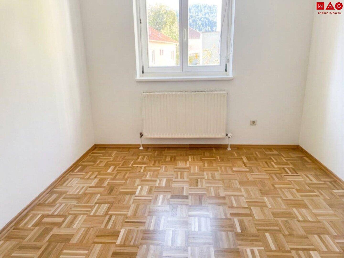 Helles Schlafzimmer mit Parkettboden und einem Fenster mit Ausblick.