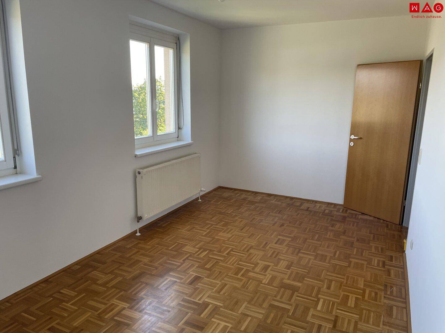 Lichtdurchflutetes Schlafzimmer mit Parkettboden und zwei Fenstern.