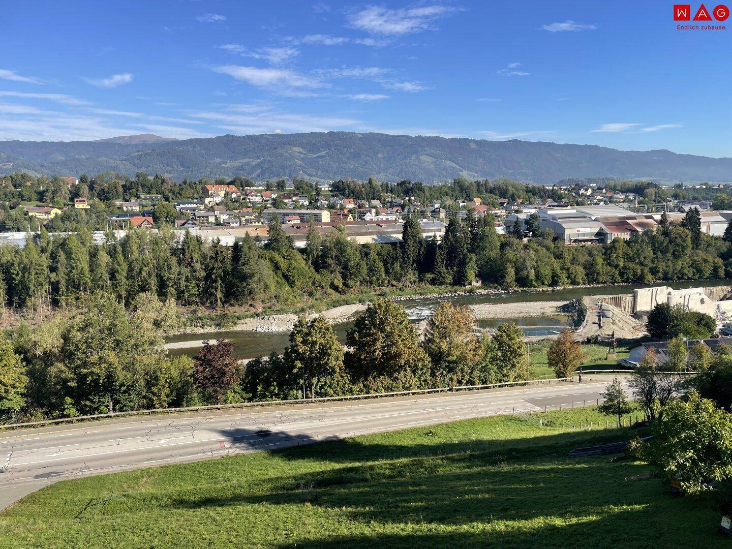 Weitläufiger Blick über die Landschaft mit Fluss, Bergen und viel Grün.