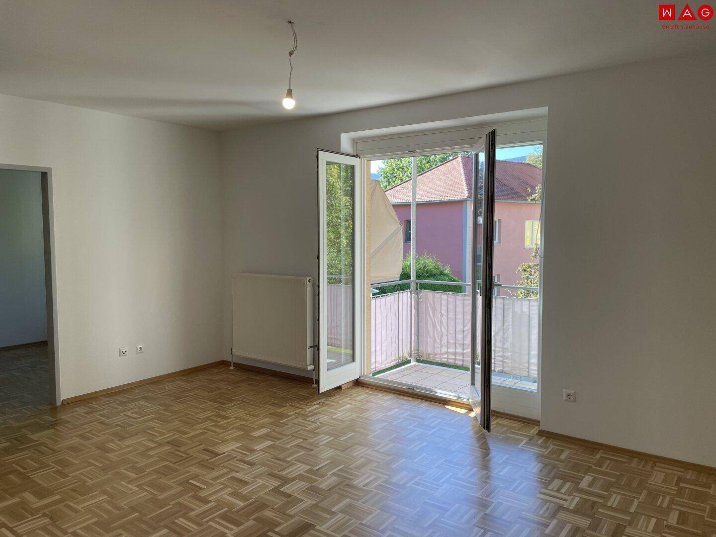 Helles Wohnzimmer mit Parkettboden und Zugang zu einem kleinen Balkon.