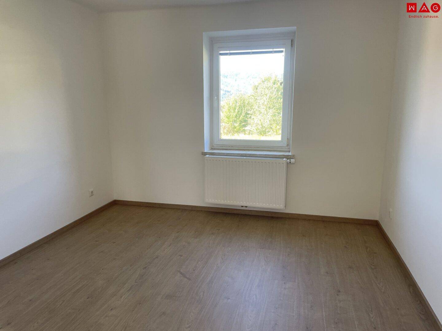 Helles Zimmer mit Laminatboden, Heizkörper und weitem Blick ins Grüne.