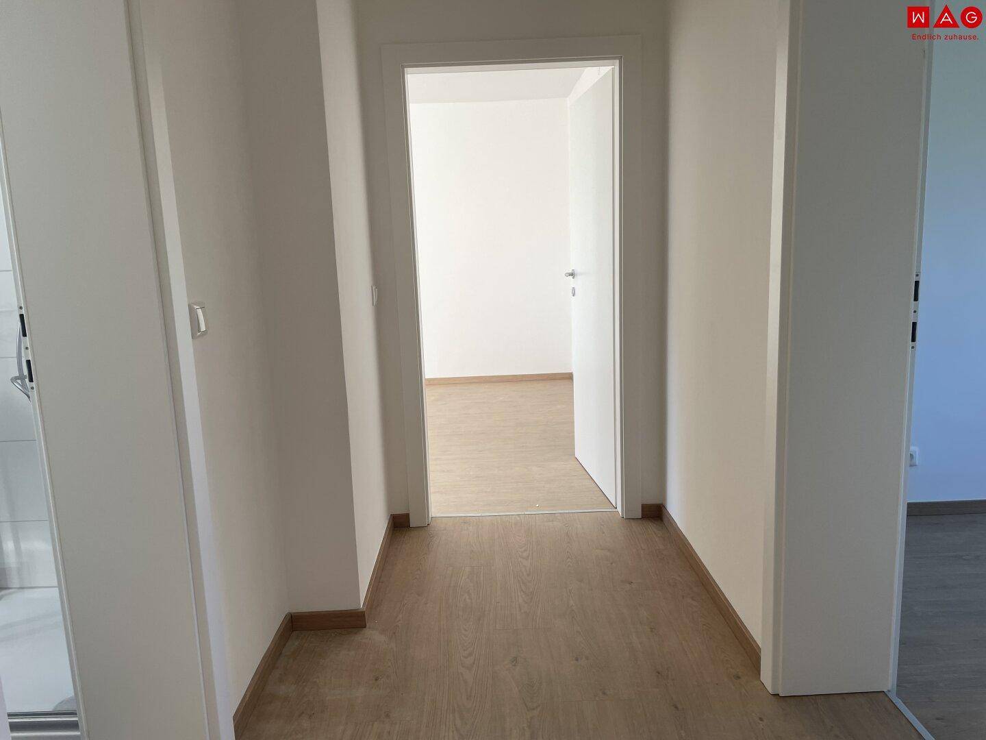 Heller Flur mit Laminatboden und offener Tür zu einem weiteren Zimmer.