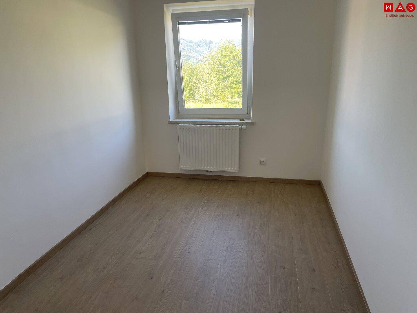 Schlafzimmer mit Laminatboden, Fenster und Blick ins Grüne.
