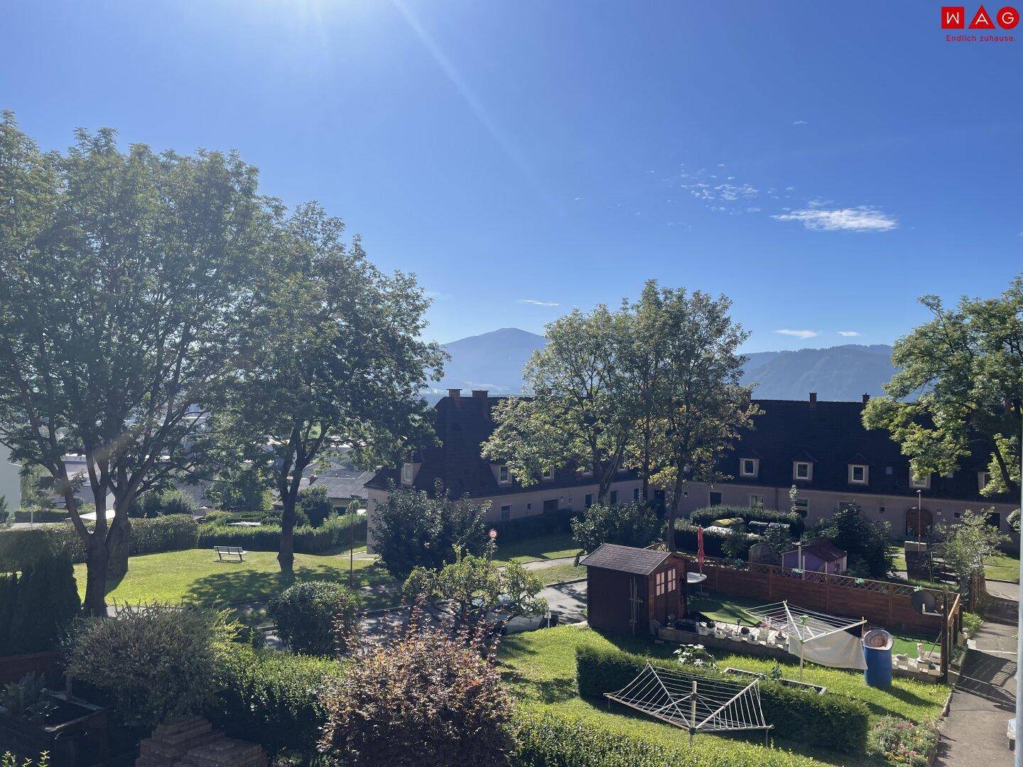 Blick auf den gepflegten Gemeinschaftsgarten mit Bäumen und Bergsicht.