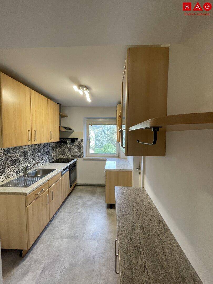 Helle Küche mit Holzschränken, gemustertem Fliesenspiegel und Fenster.