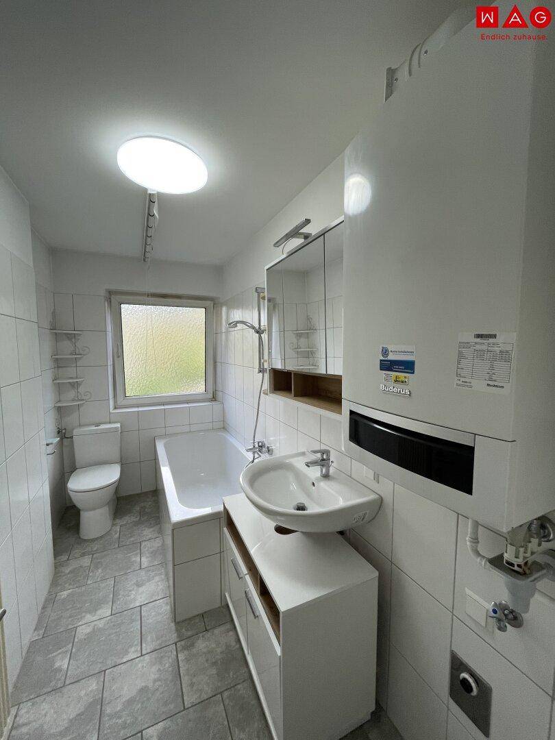 Badezimmer mit Badewanne, Waschbecken, Toilette und Fenster, hell gefliest.