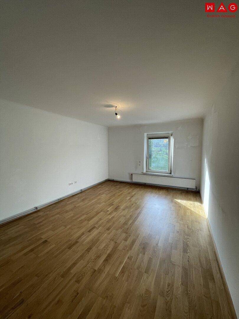 Geräumiges, leeres Zimmer mit hellem Parkettboden und einem Fenster.