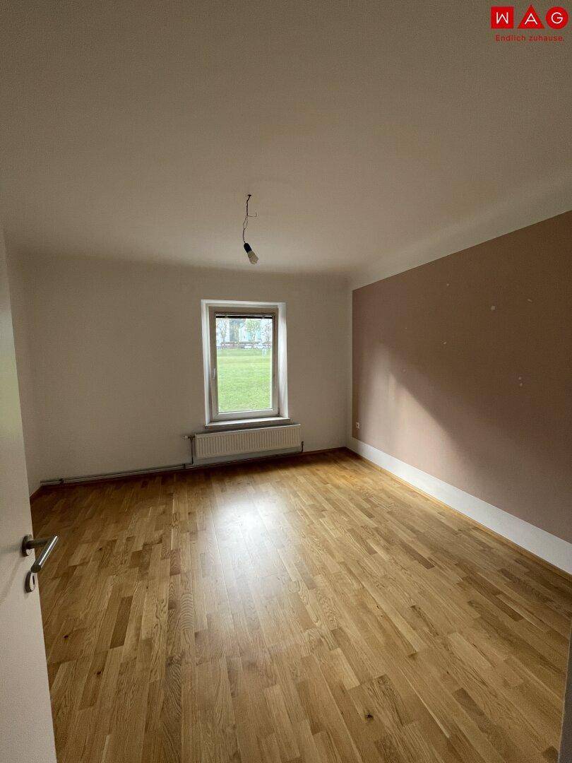 Leeres Zimmer mit Parkettboden, Fenster und einer Wand in warmem Rosaton.