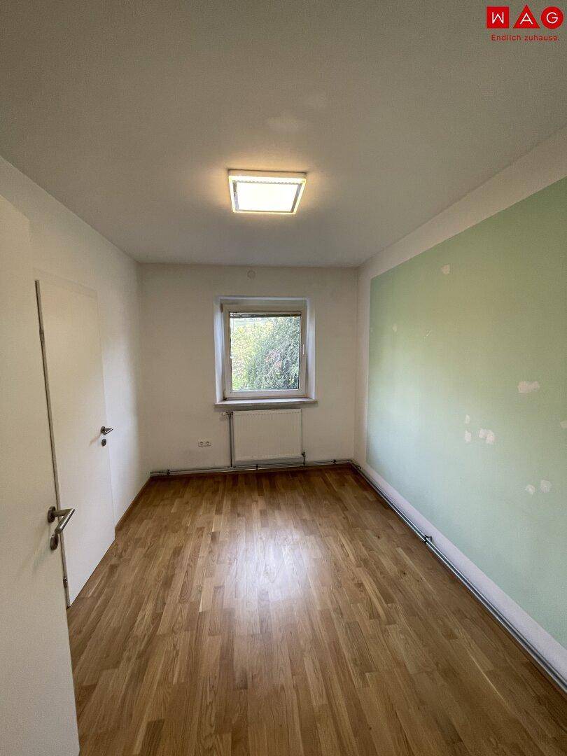 Helles Schlafzimmer mit Parkettboden, Fenster und einer Wand in Grün.