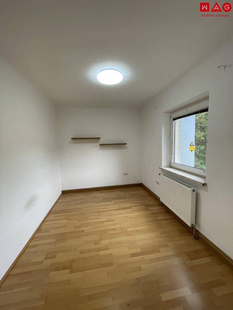 Leerer Raum mit Parkettboden, Fenster und schwebenden Wandregalen, ideal für ein Kinderzimmer.