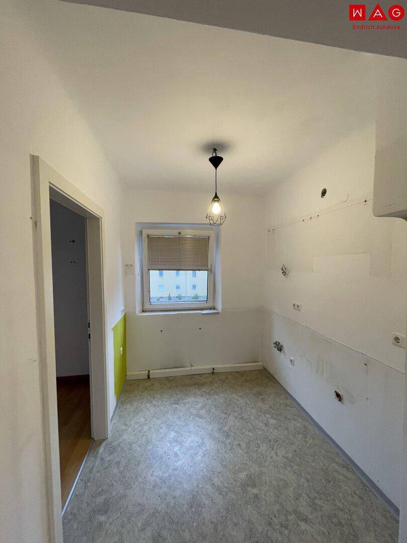 Leere Küchenzeile mit Fenster und Anschlüssen, bereit für eine neue Einbauküche.