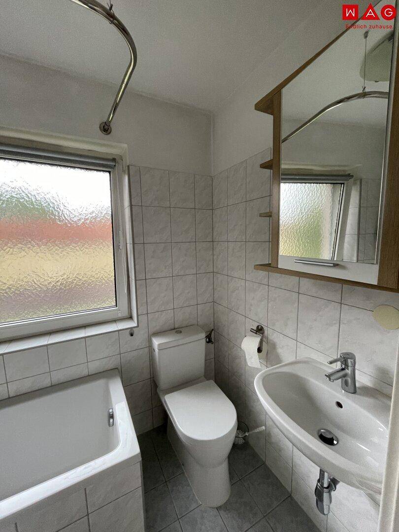 Helles Badezimmer mit Badewanne, WC, Waschbecken und weißen Fliesen.