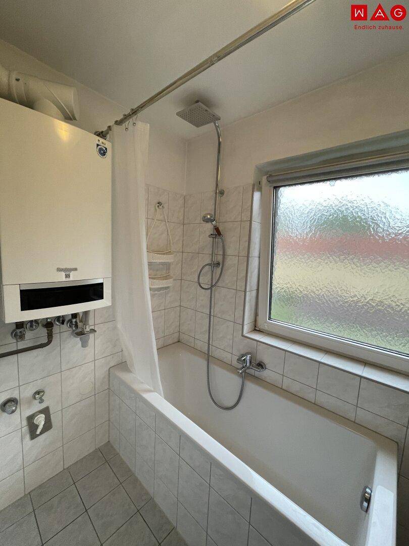 Funktionales Badezimmer mit Badewanne, Duschvorrichtung und Warmwasserboiler.