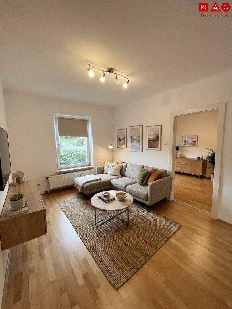 Gemütliches Wohnzimmer mit modernem Sofa, Holzboden und Blick ins Grüne.