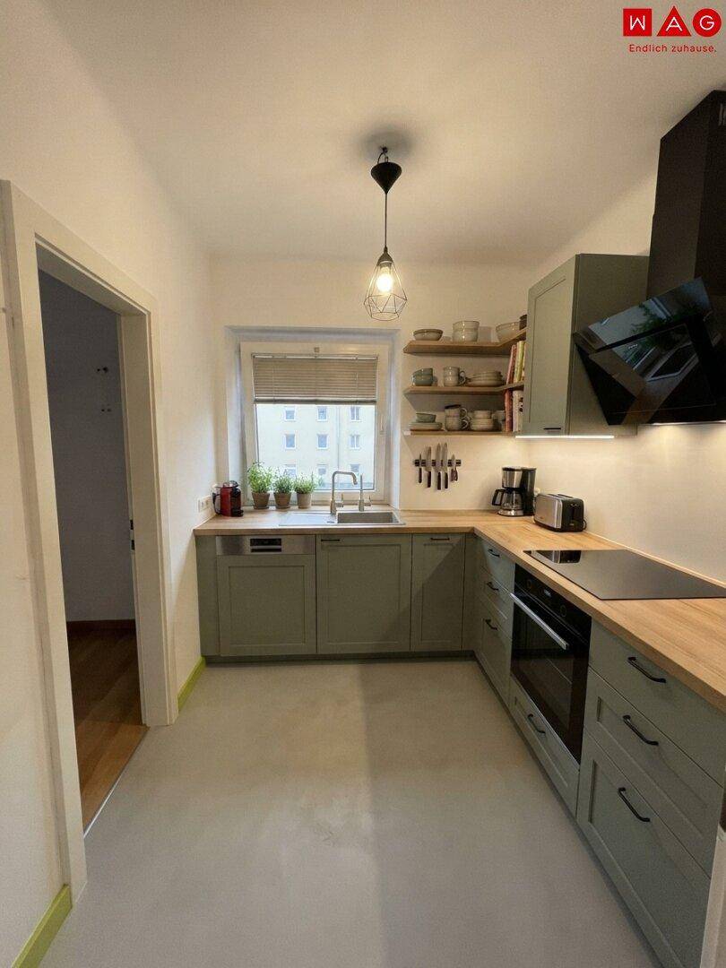 Moderne Küche mit grünen Schränken, Holzarbeitsplatte und integrierten Geräten.