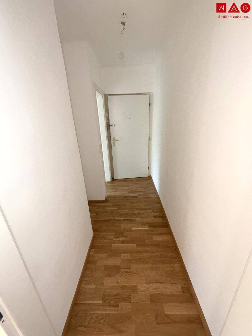 Langer Flur mit Parkettboden und weißen Wänden, der zu weiteren Räumen führt.