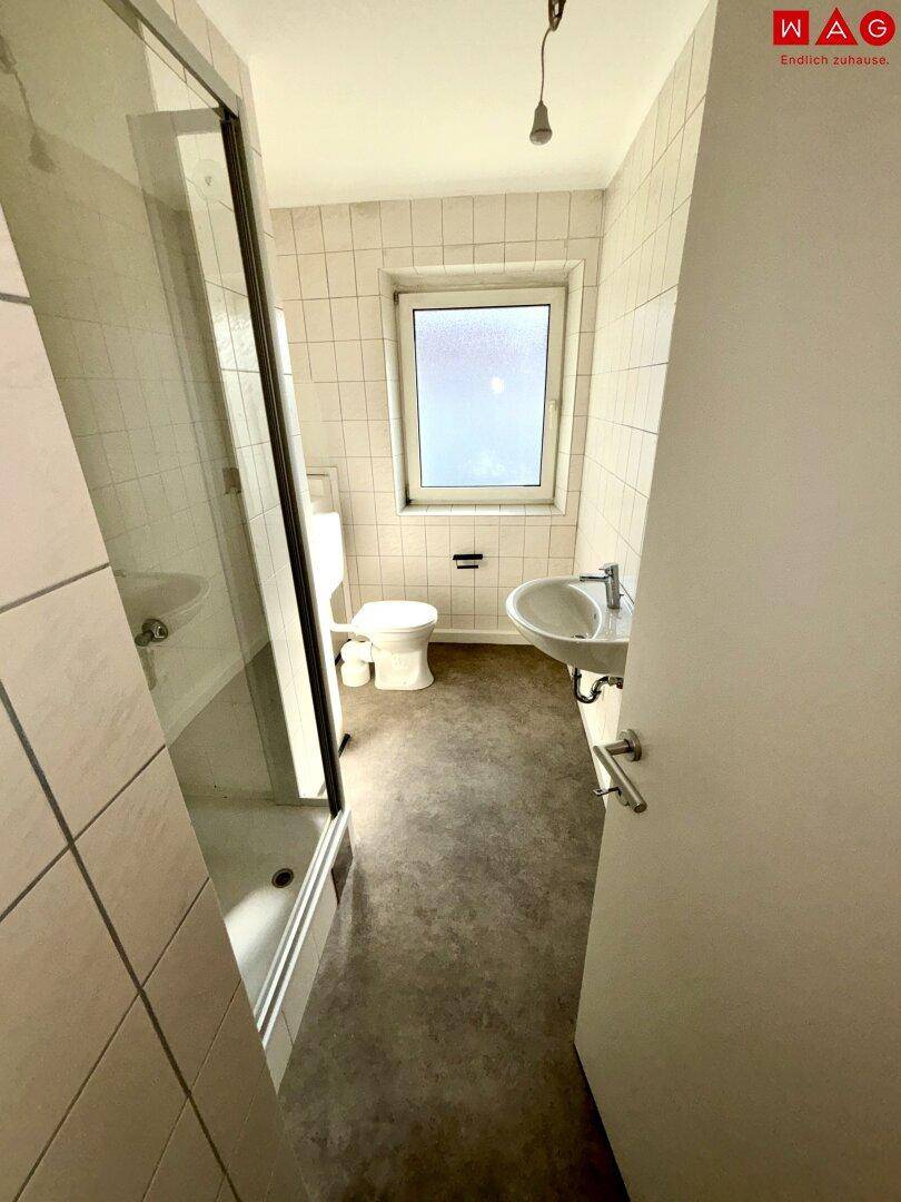 Funktionales Badezimmer mit Dusche, WC, Waschbecken und Fenster, hell gefliest.