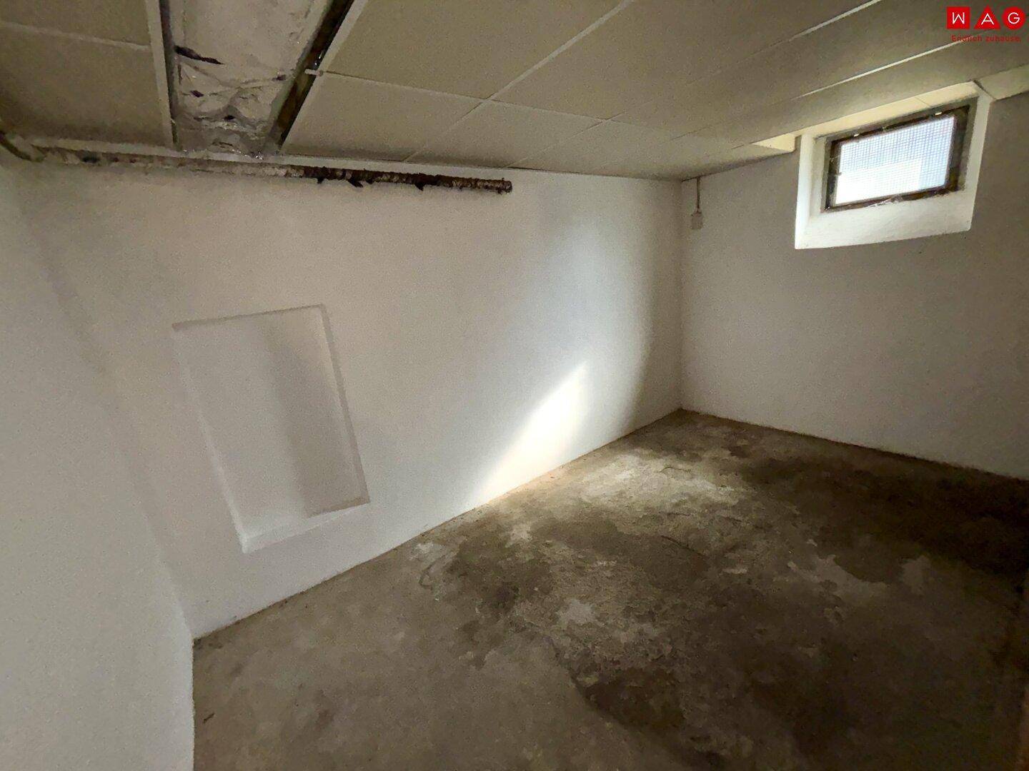 Einfacher Kellerraum mit Betonboden und kleinem Fenster, ideal als Abstellfläche.