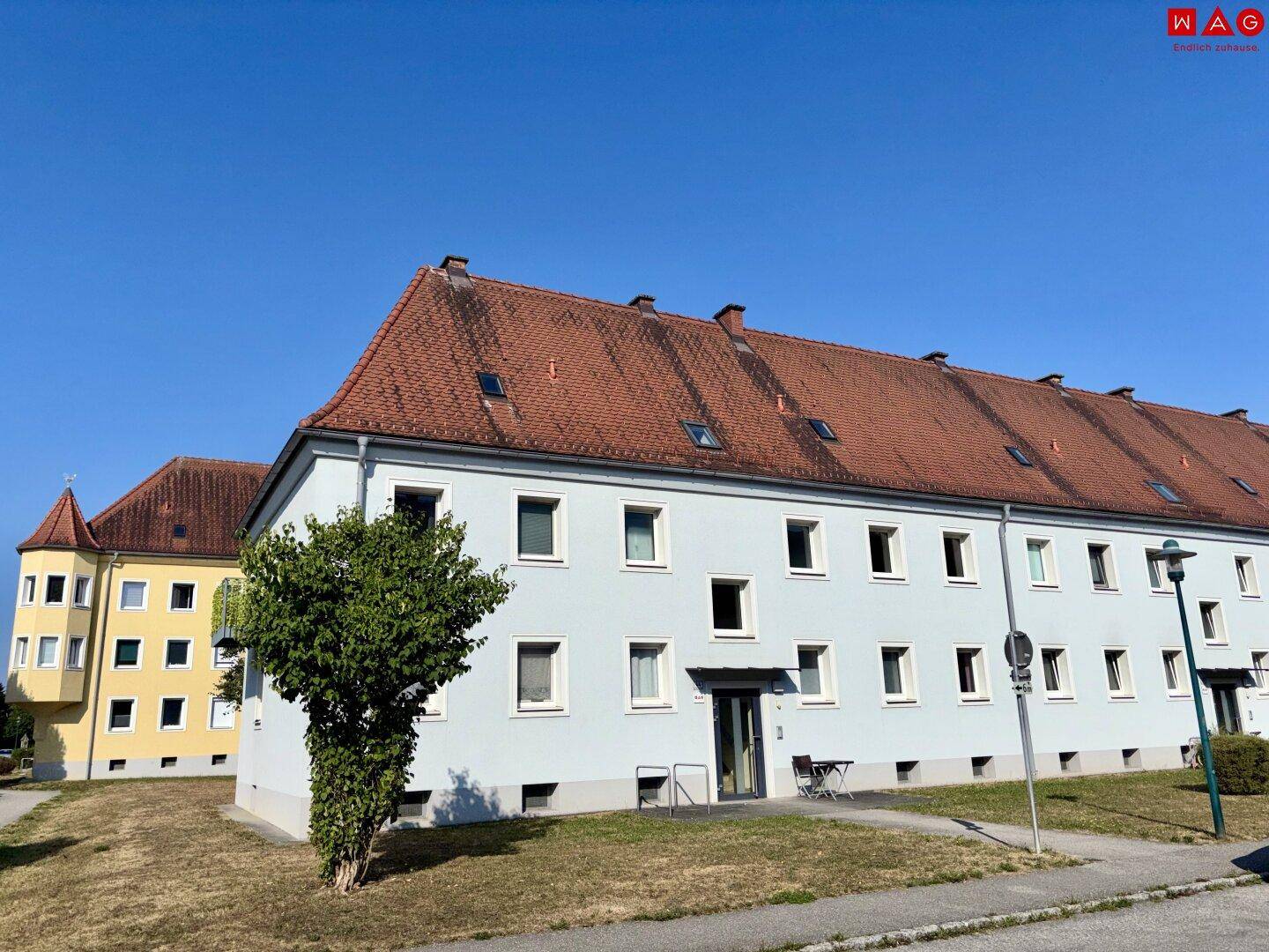 Mehrfamilienhaus mit traditionellem Satteldach und mehreren Fenstern in sonniger Umgebung.