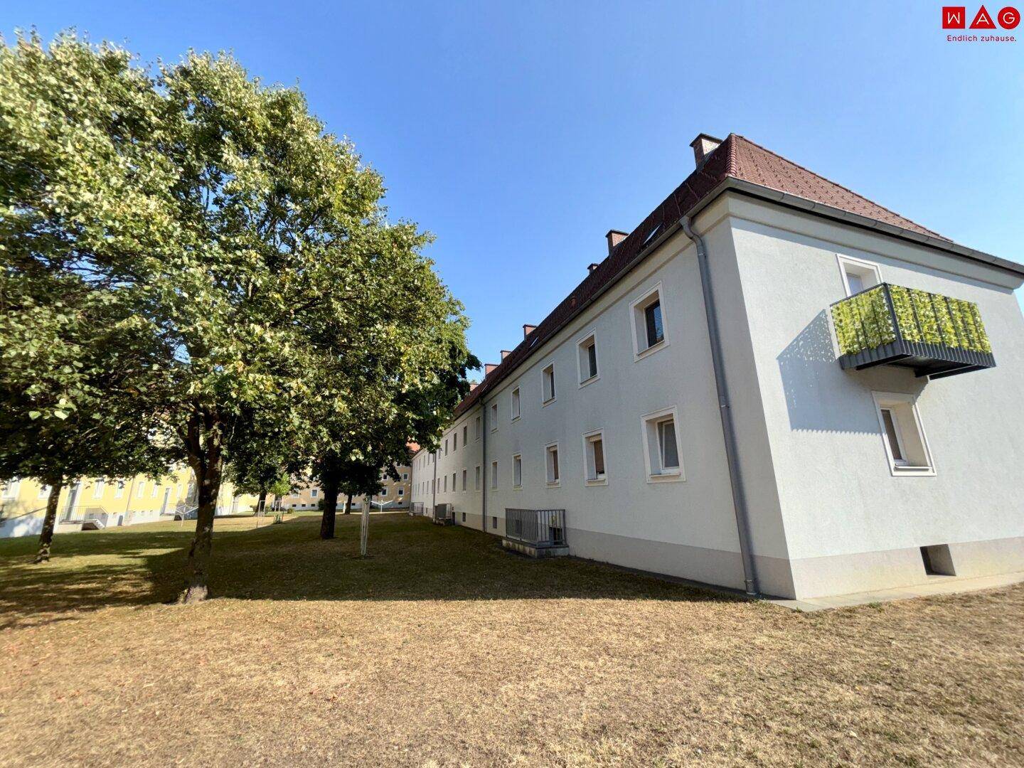 Seitenansicht eines Wohngebäudes mit Balkon und gepflegter Grünfläche im Vordergrund.