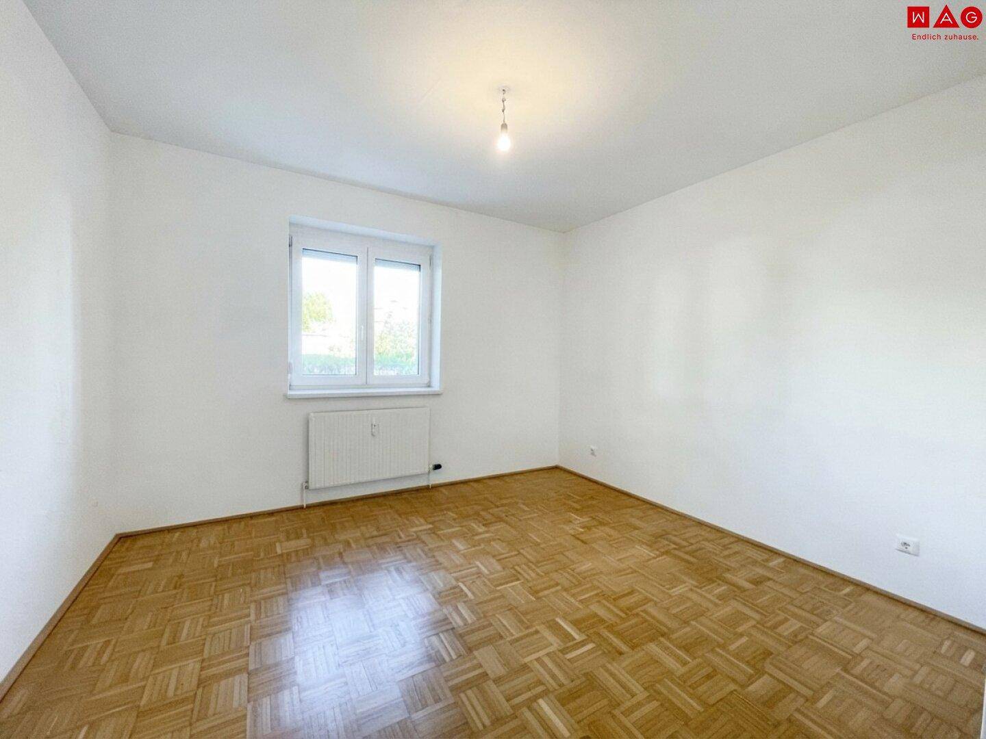 Leeres Schlafzimmer mit Parkettboden und Fenster, bietet viel Gestaltungspotenzial.