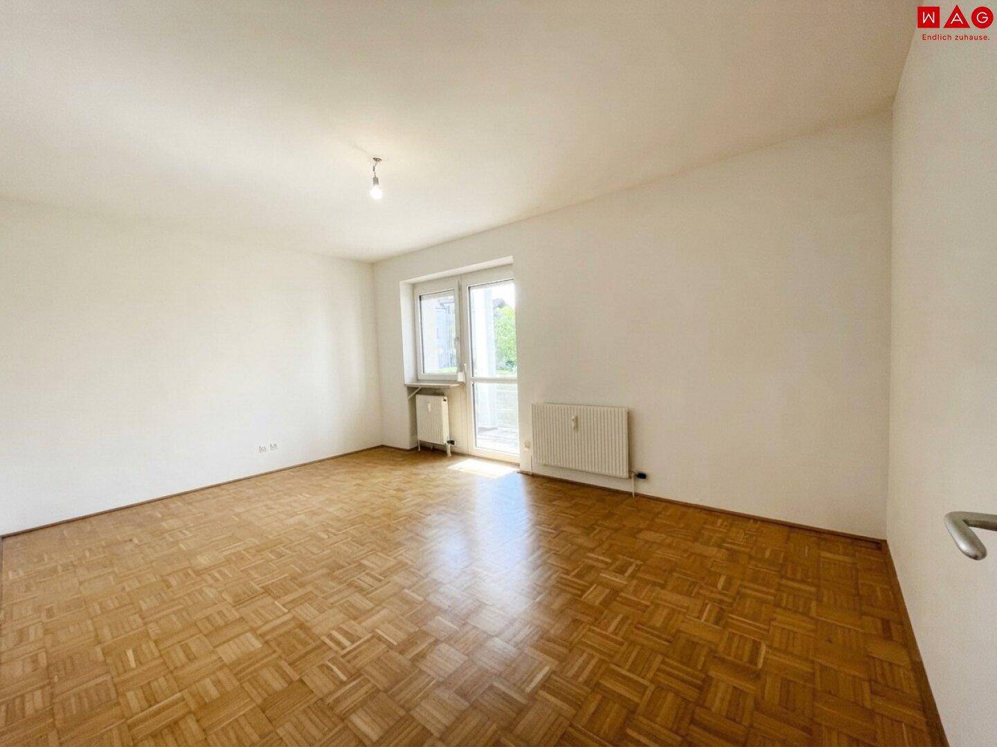 Helles Wohnzimmer mit Parkettboden und Zugang zu einem Außenbereich.