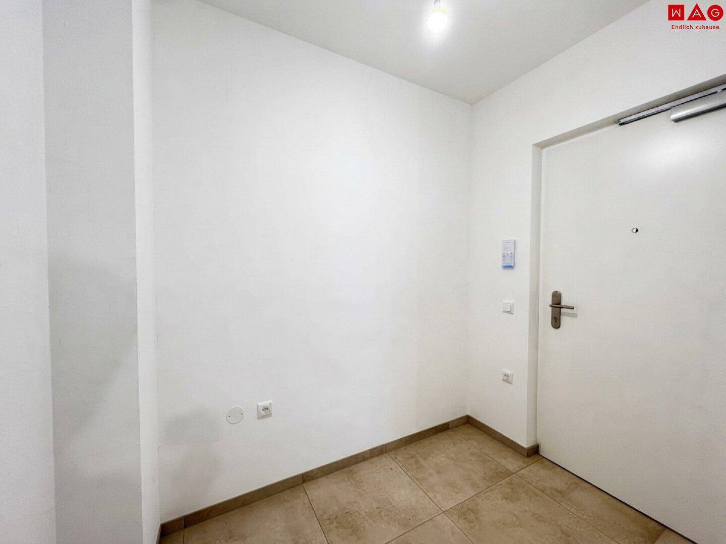 Eingangsbereich mit Fliesenboden und weißer Eingangstür, die in die Wohnung führt.
