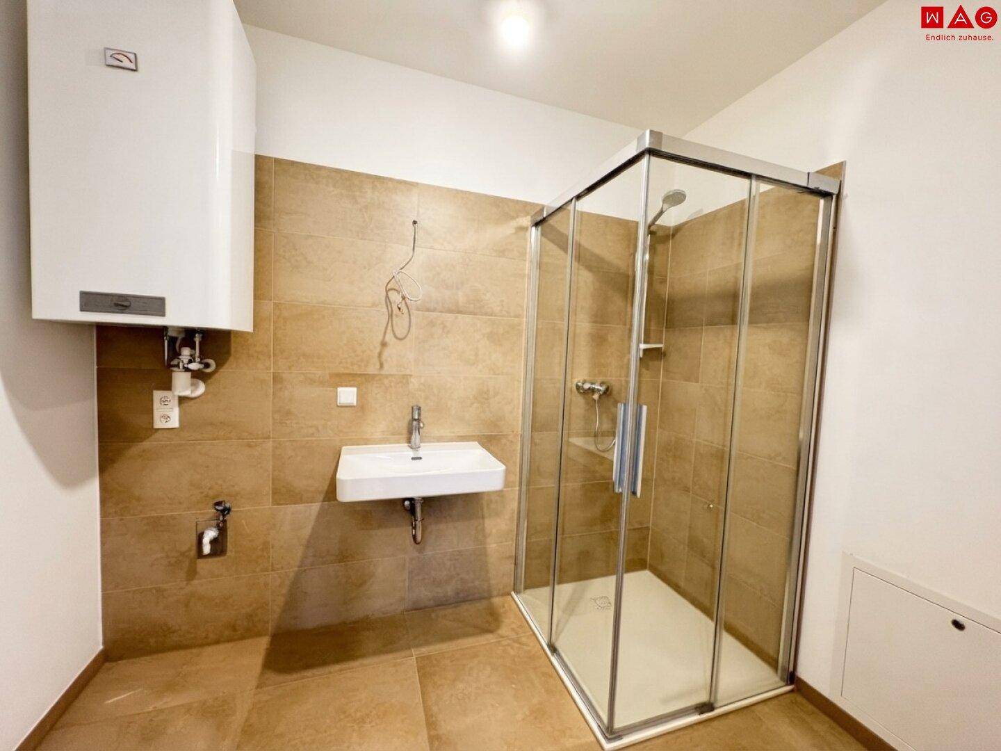 Modernes Badezimmer mit Duschkabine, Waschbecken und beigefarbenen Fliesen an Wänden und Boden.