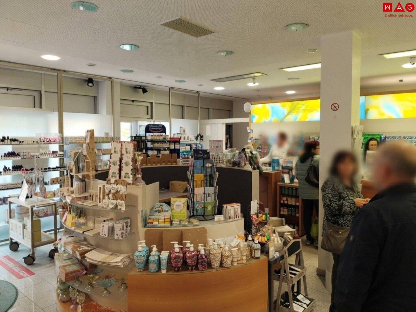 Heller Verkaufsraum einer Apotheke mit Kunden, Regalen und einer breiten Produktauswahl.