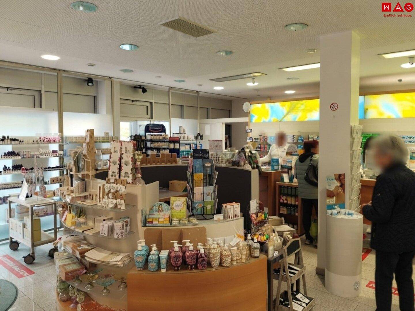 Offener Verkaufsbereich einer Apotheke mit runden Präsentationstischen und Kunden.