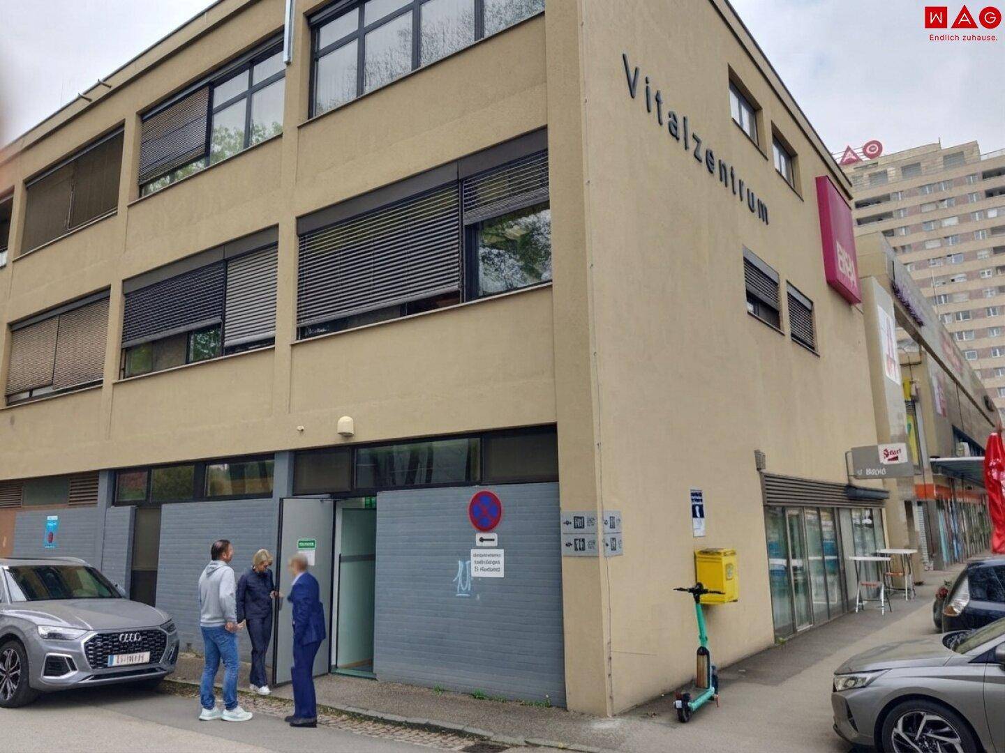 Seitenansicht des Vitalzentrums mit mehreren Fenstern und Personen vor dem Eingangsbereich.