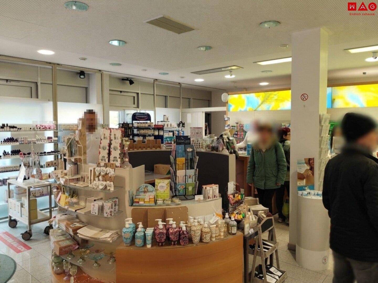 Verkaufsbereich einer Apotheke mit verschiedenen Produktpräsentationen und Kunden im Hintergrund.