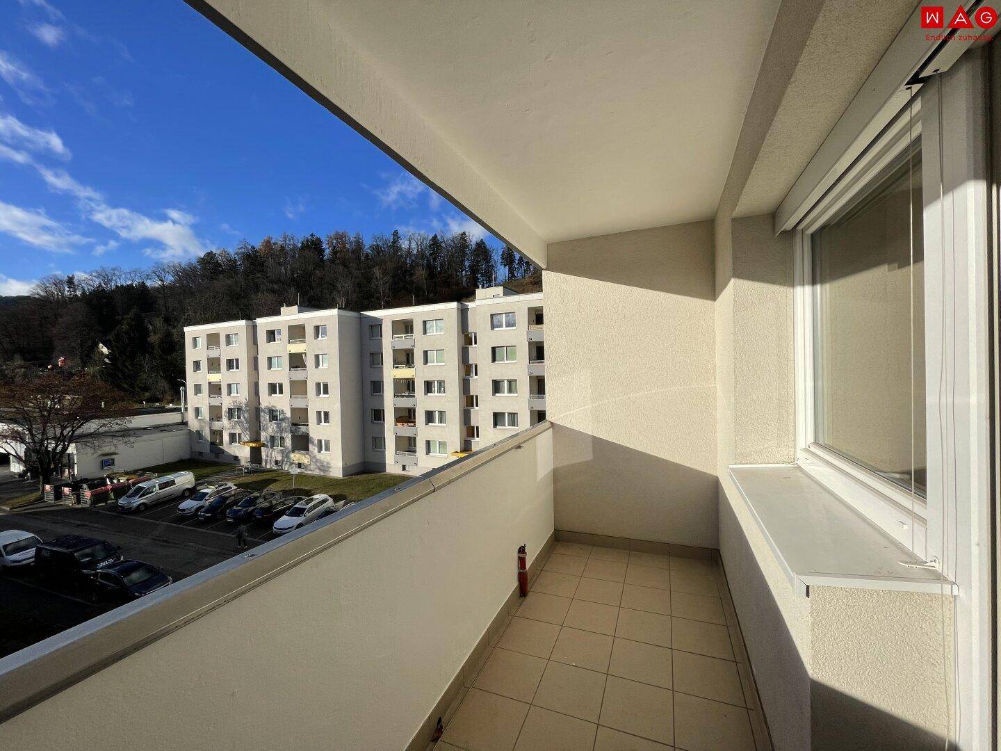Heller Balkon mit Fliesenboden und Blick auf die umliegenden Gebäude und bewaldete Hügel.