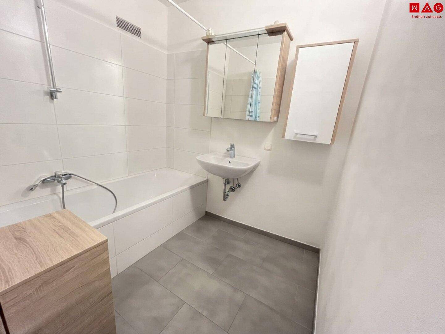 Helles Badezimmer mit Badewanne, Waschbecken und Spiegelschrank, ausgestattet mit modernen Fliesen.