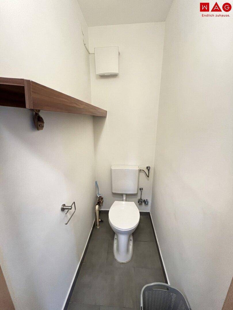 Separates WC mit Toilette und dunklem Fliesenboden, praktisch und funktional gestaltet.