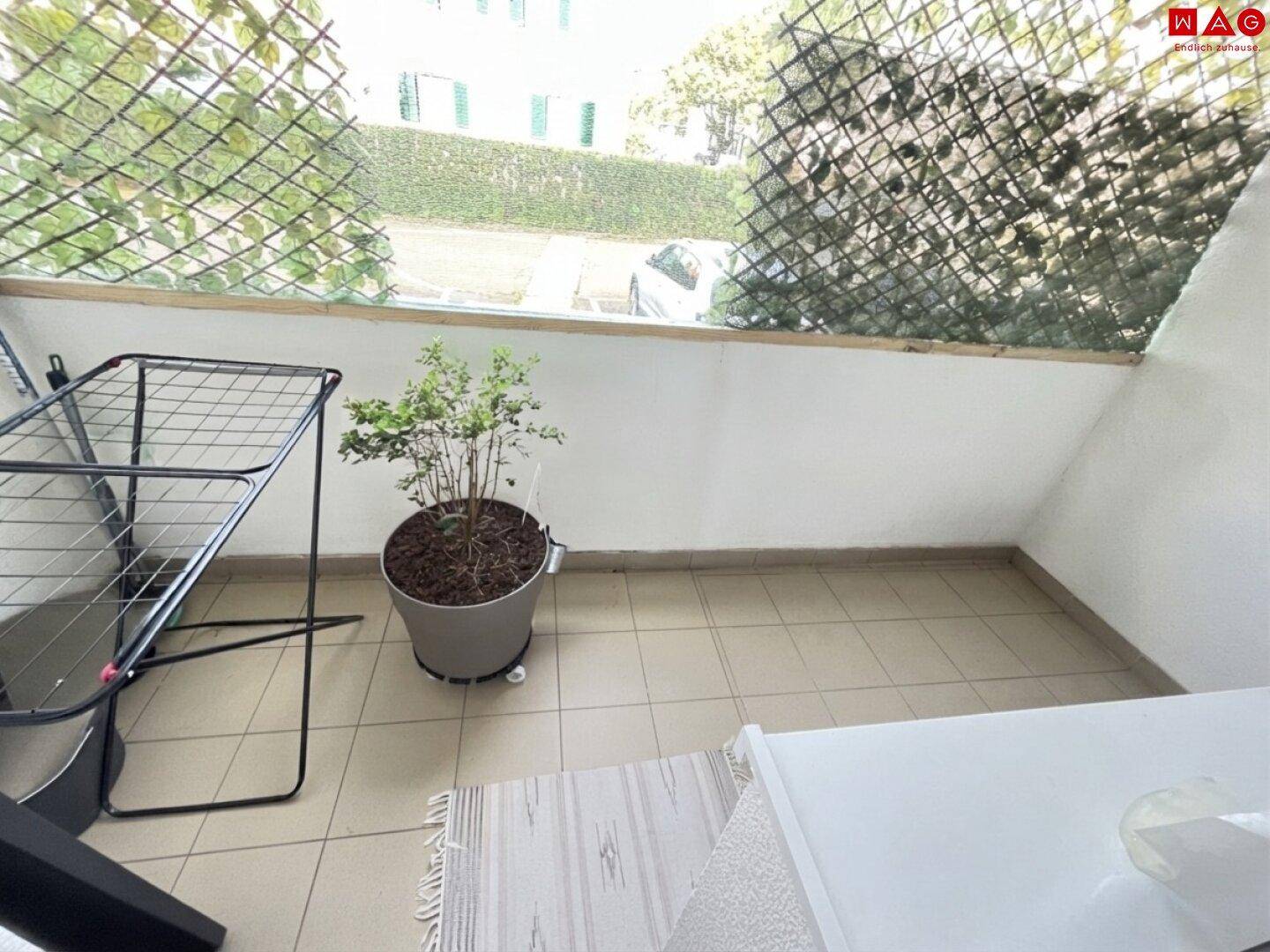 Kleiner Balkon mit Fliesenboden, Wäscheständer und Blick ins Grüne.