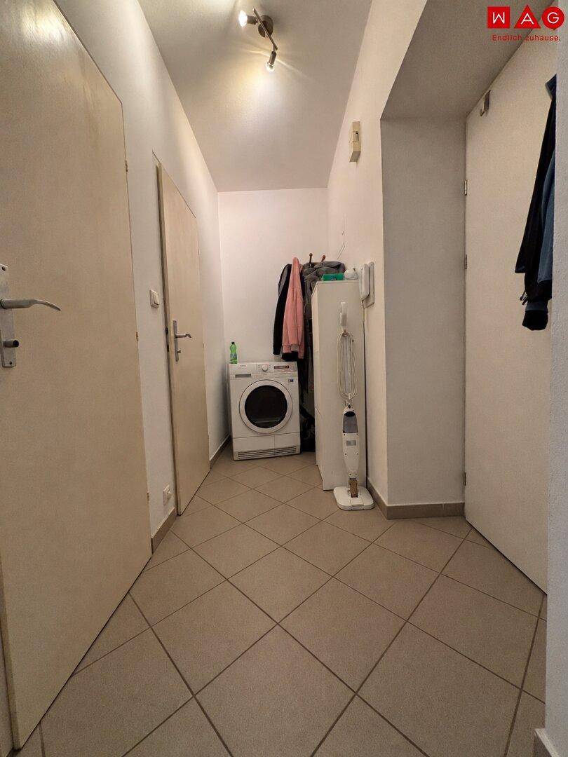 Heller Flur mit Fliesenboden und Platz für eine Waschmaschine, der zu den weiteren Räumen führt.
