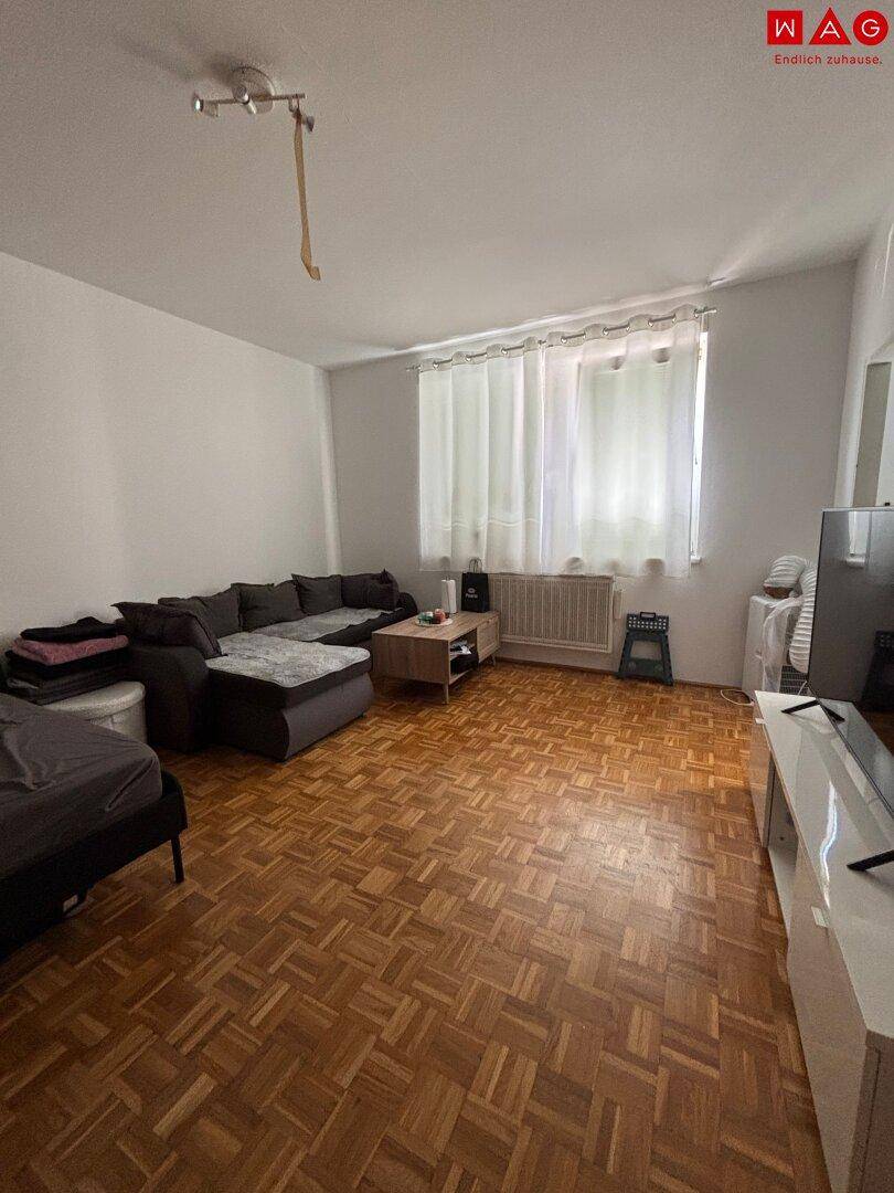 Gemütliches Wohnzimmer mit Parkettboden, Sofa und Fenster, das viel Tageslicht hereinlässt.