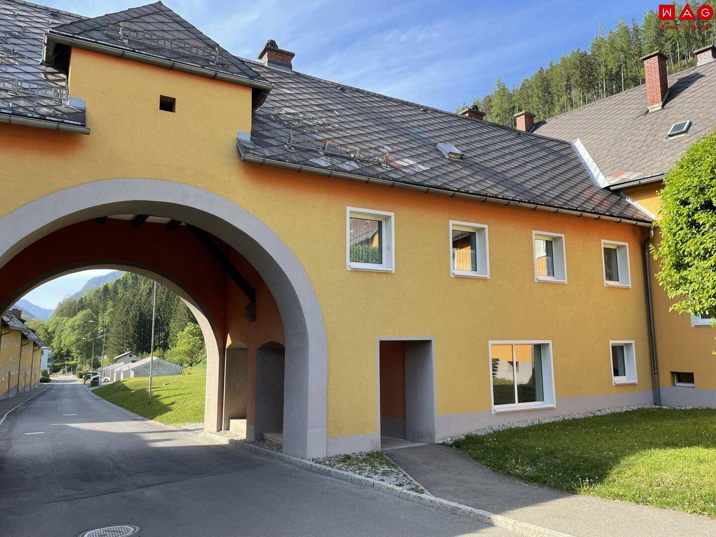 Detailansicht eines gelben Gebäudes mit einem großen Torbogen und dunklem Ziegeldach in ländlicher Umgebung.