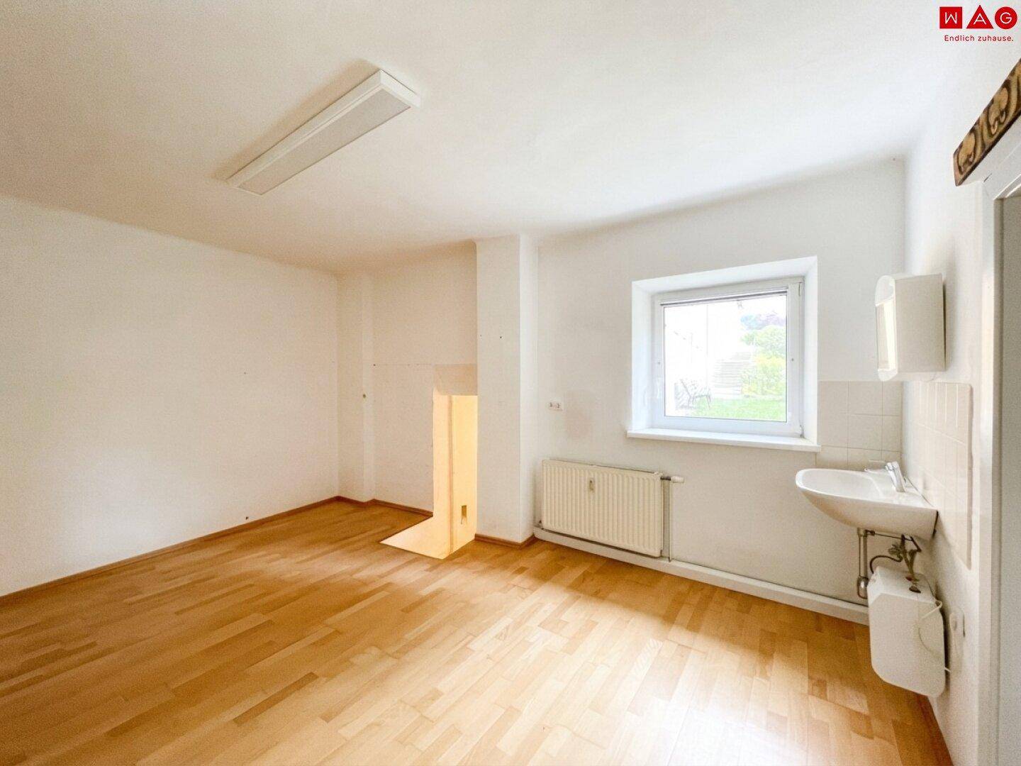 Heller Raum mit Holzboden, weißem Waschbecken und einem Fenster, ideal als Büro oder Nebenraum.