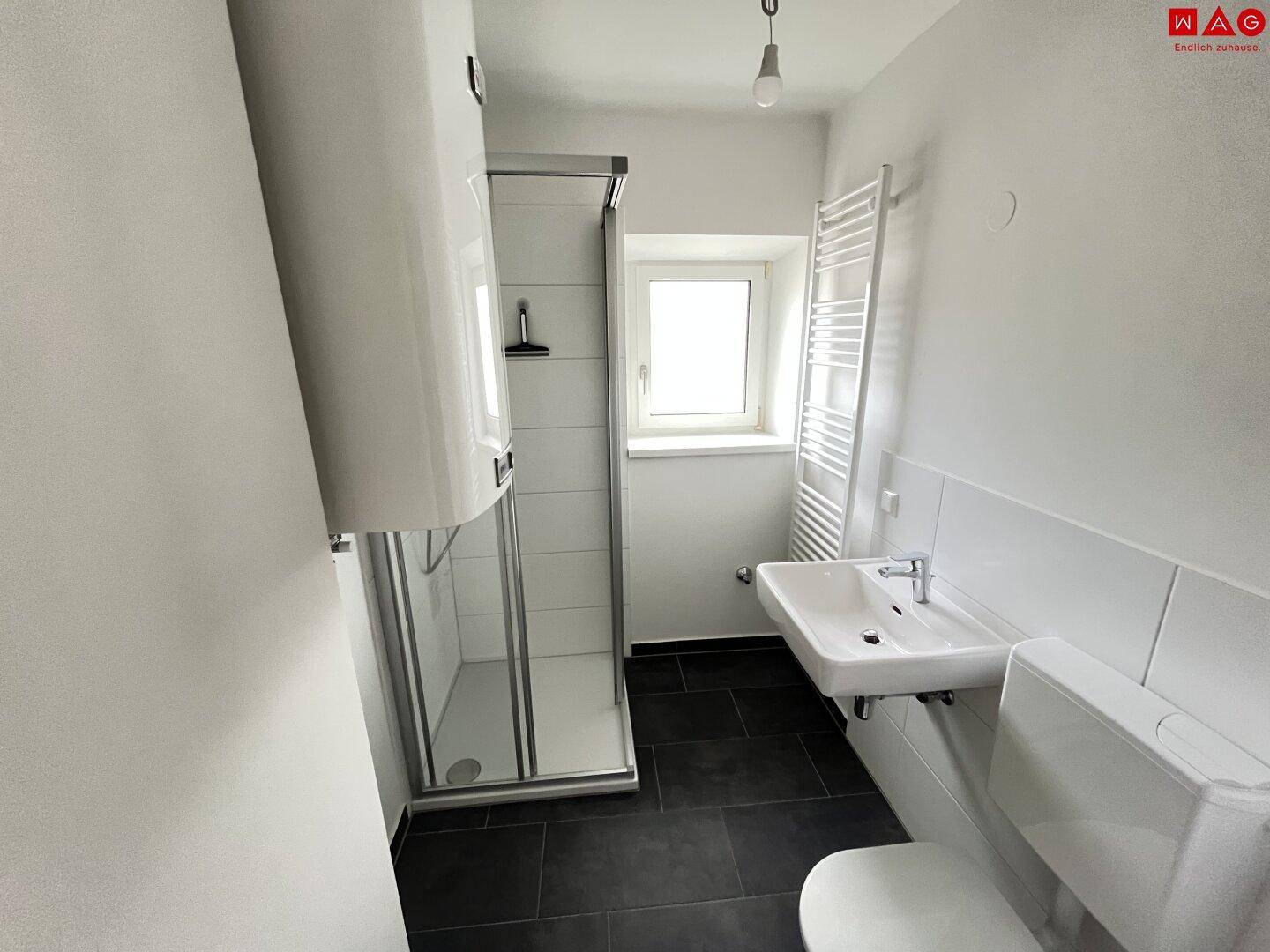 Modernes Badezimmer mit Dusche, Waschbecken, WC und dunklen Fliesen, ausgestattet mit einem Handtuchheizkörper.