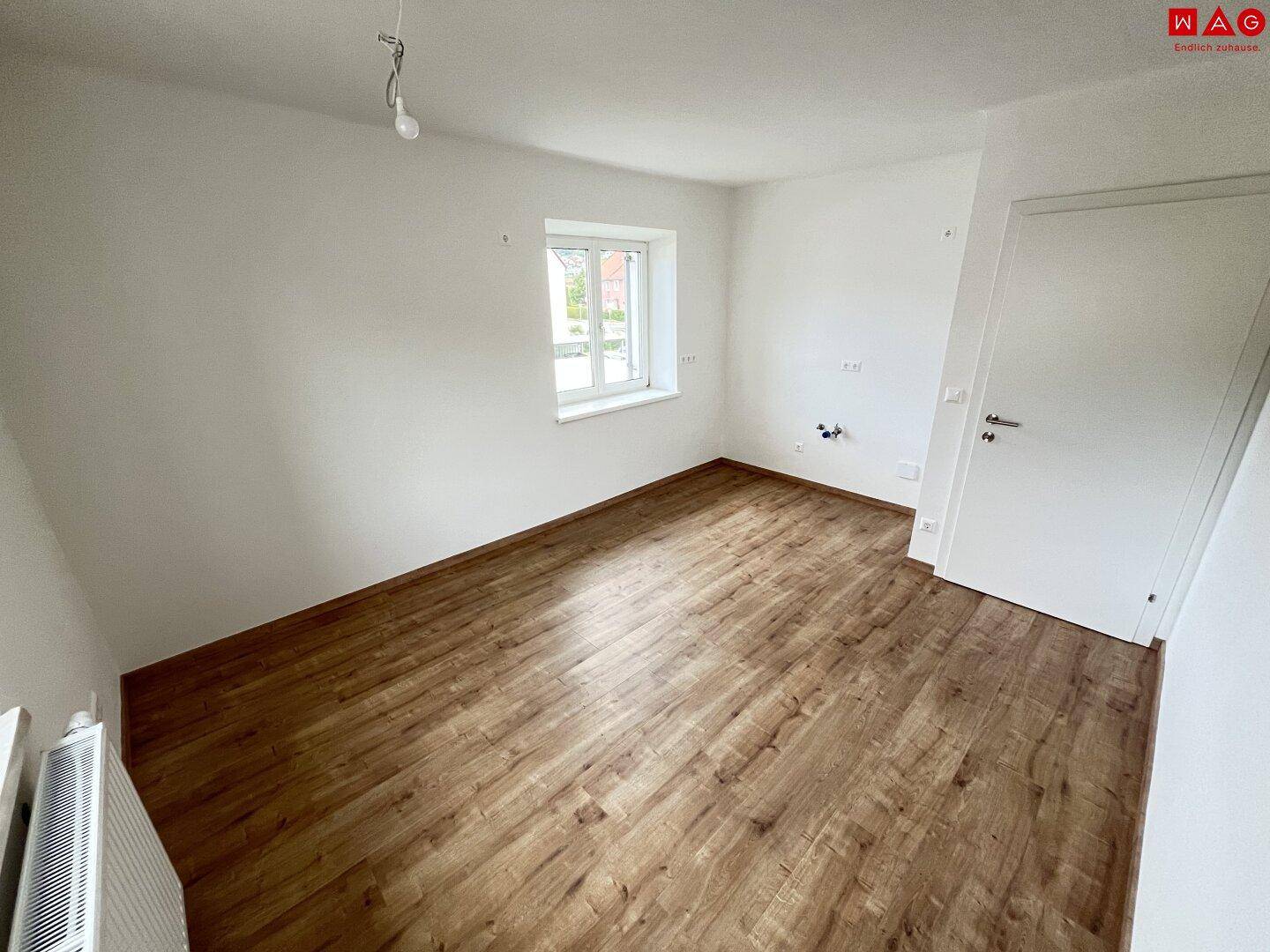 Helles Zimmer mit neuem Laminatboden, weißen Wänden und einem Fenster mit Blick nach draußen.