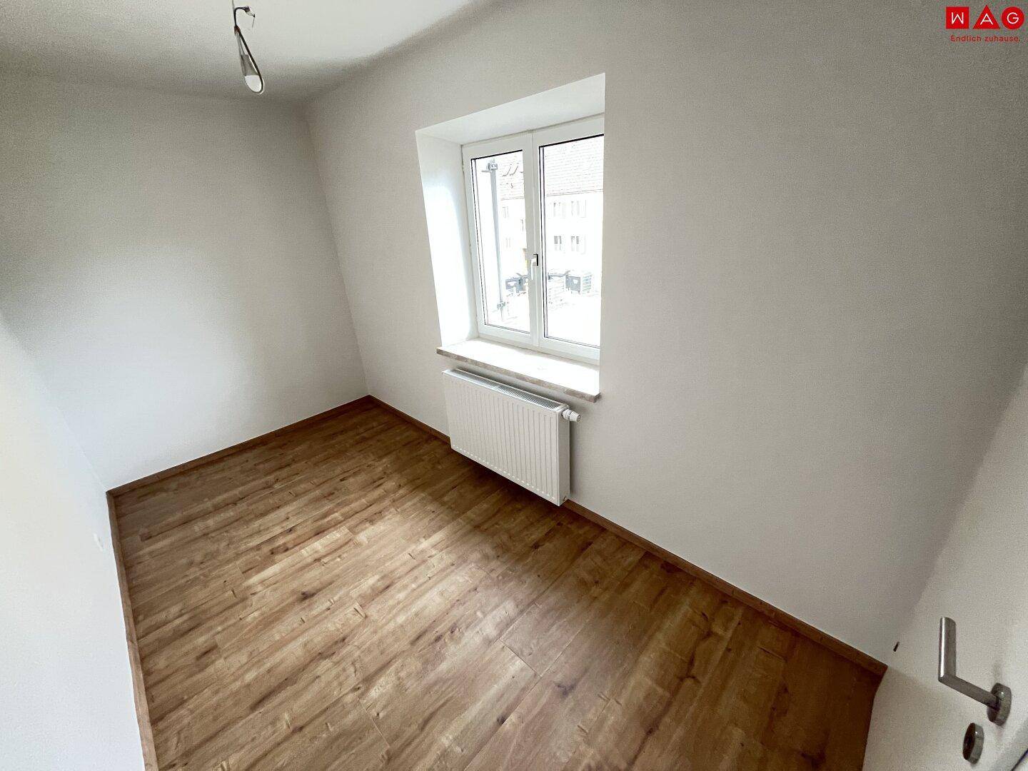 Freundliches Zimmer mit Laminatboden, weißen Wänden und einem großen Fenster für viel Tageslicht.