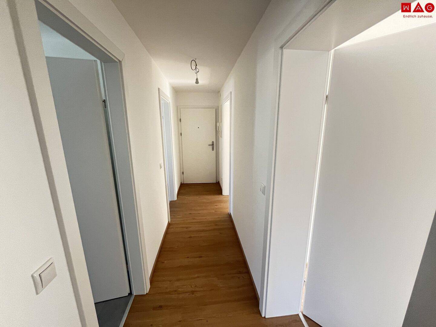 Heller Flur mit Parkettboden und weißen Türen, der zu verschiedenen Räumen der Wohnung führt.