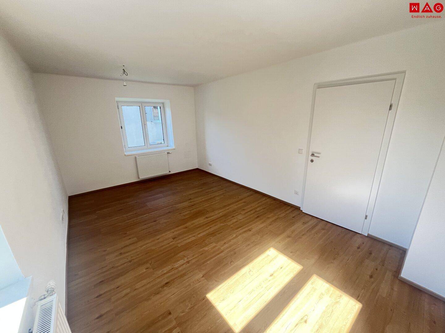 Geräumiger, heller Raum mit Holzboden, weißen Wänden und einer modernen Tür, ideal für Wohnzwecke.