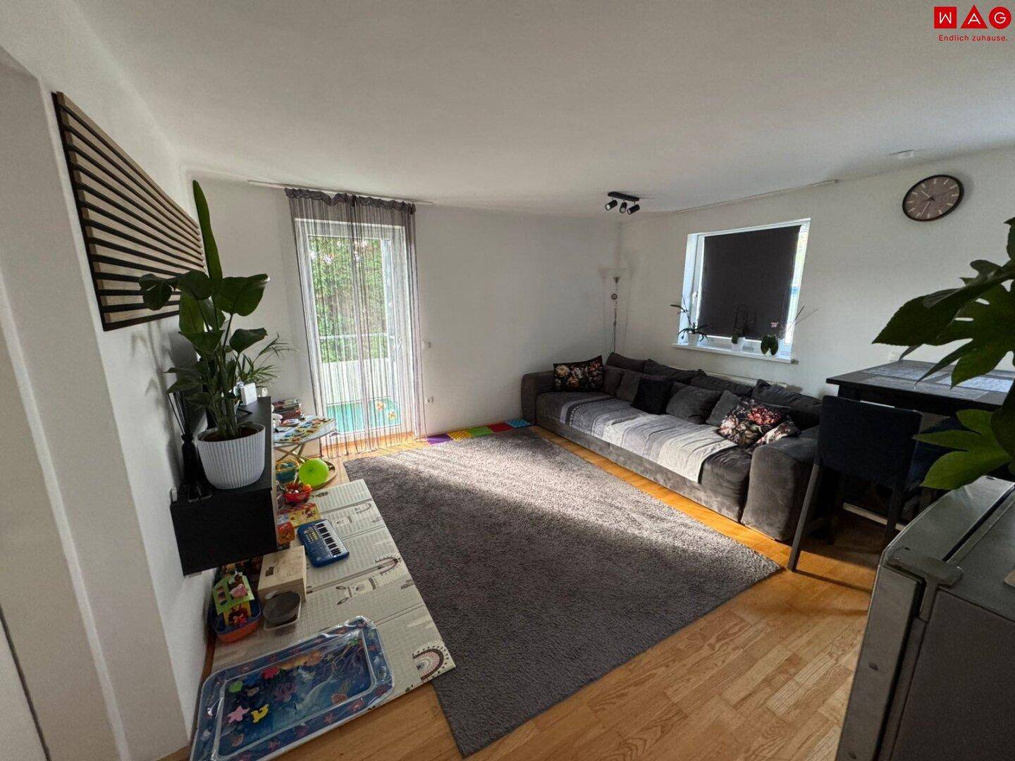 Helles Wohnzimmer mit großem Sofa, Holzboden und Zugang zu einem Balkon, ideal für Entspannung.