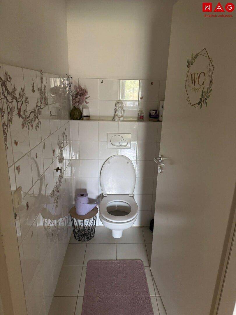 Separate Toilette mit WC, kleinen Fliesen und einem Fenster, dekoriert mit floralen Elementen.